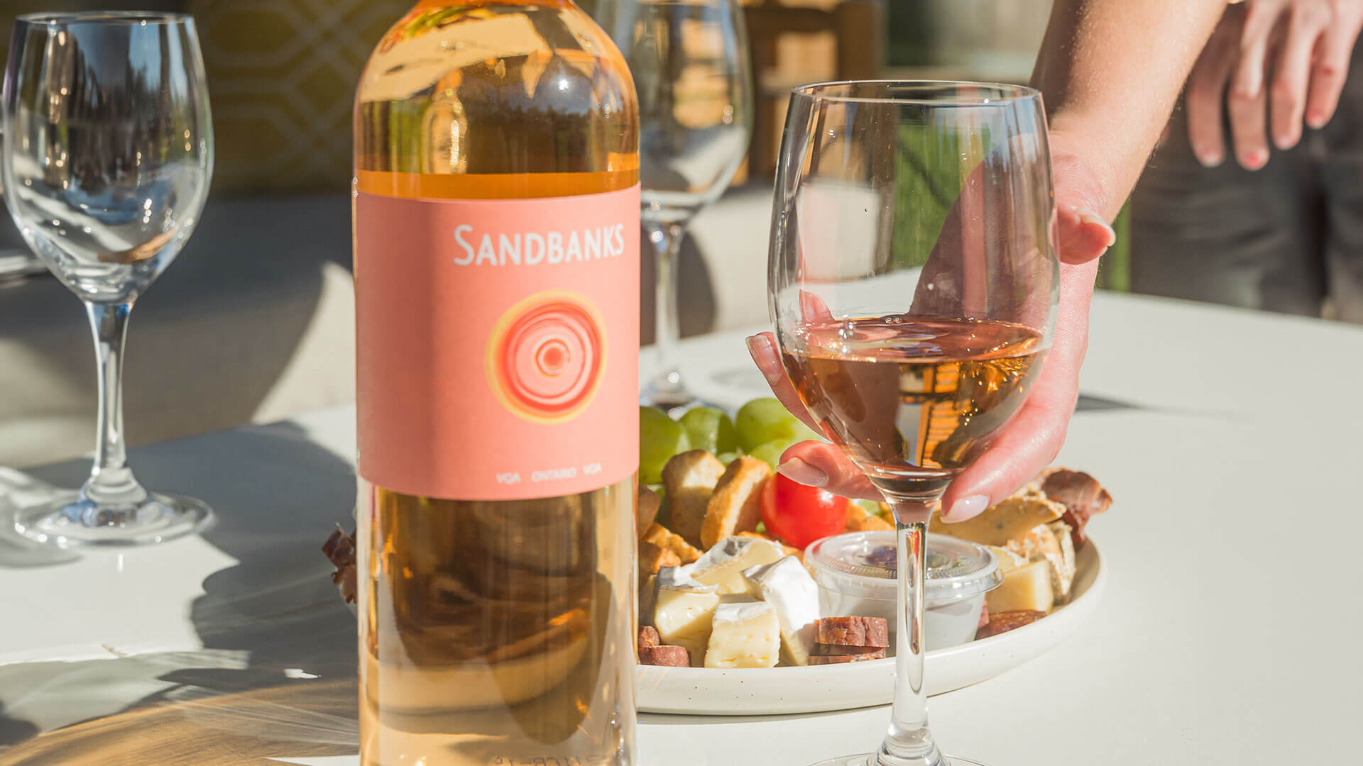 Women holding glass of Sandbanks Rosé with the bottle next to her.