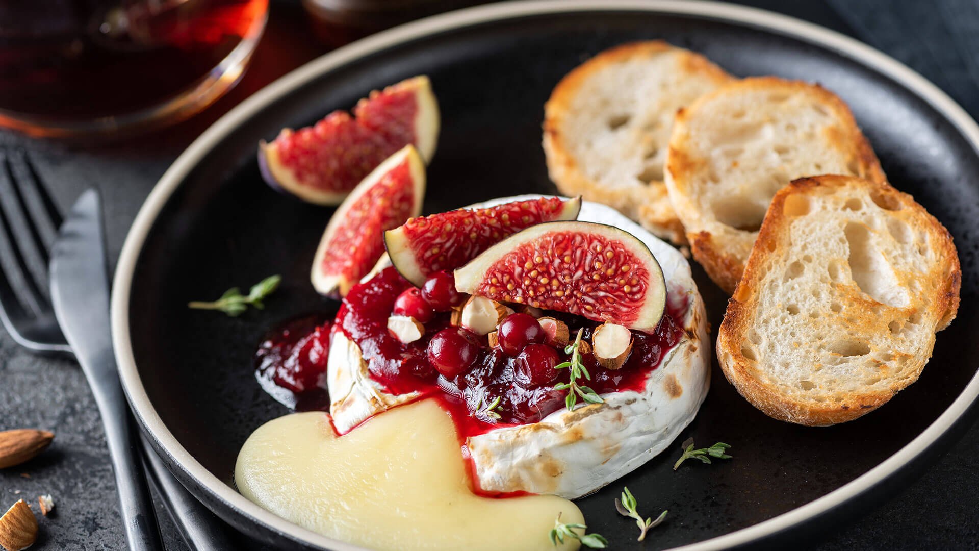 A plate of Brie Cheese, bread, red pepper jelly, and figs paired with a glass of red wine.