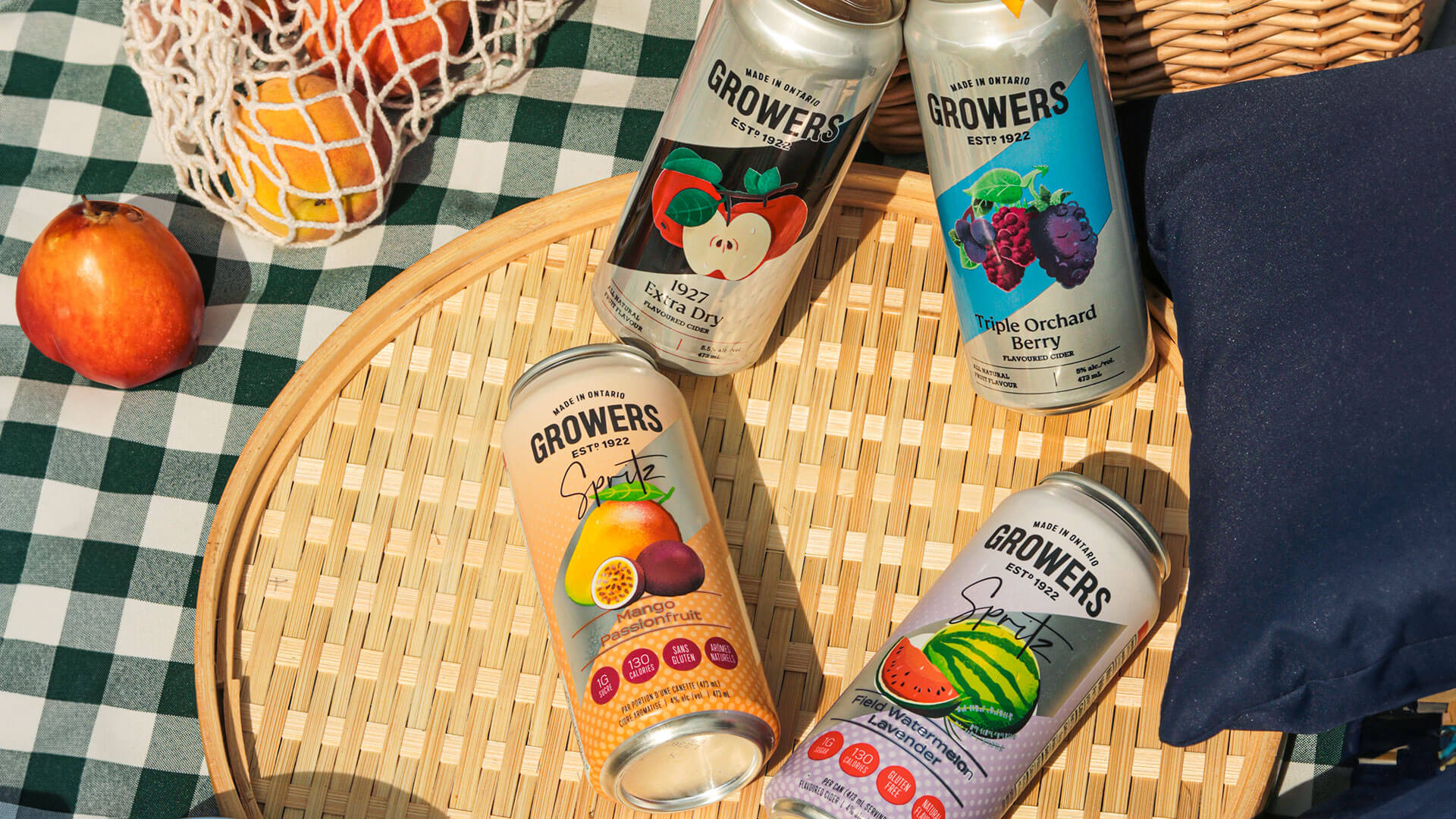 Growers Ciders Variety on a picnic table with peaches, pretzels, and sunflowers.