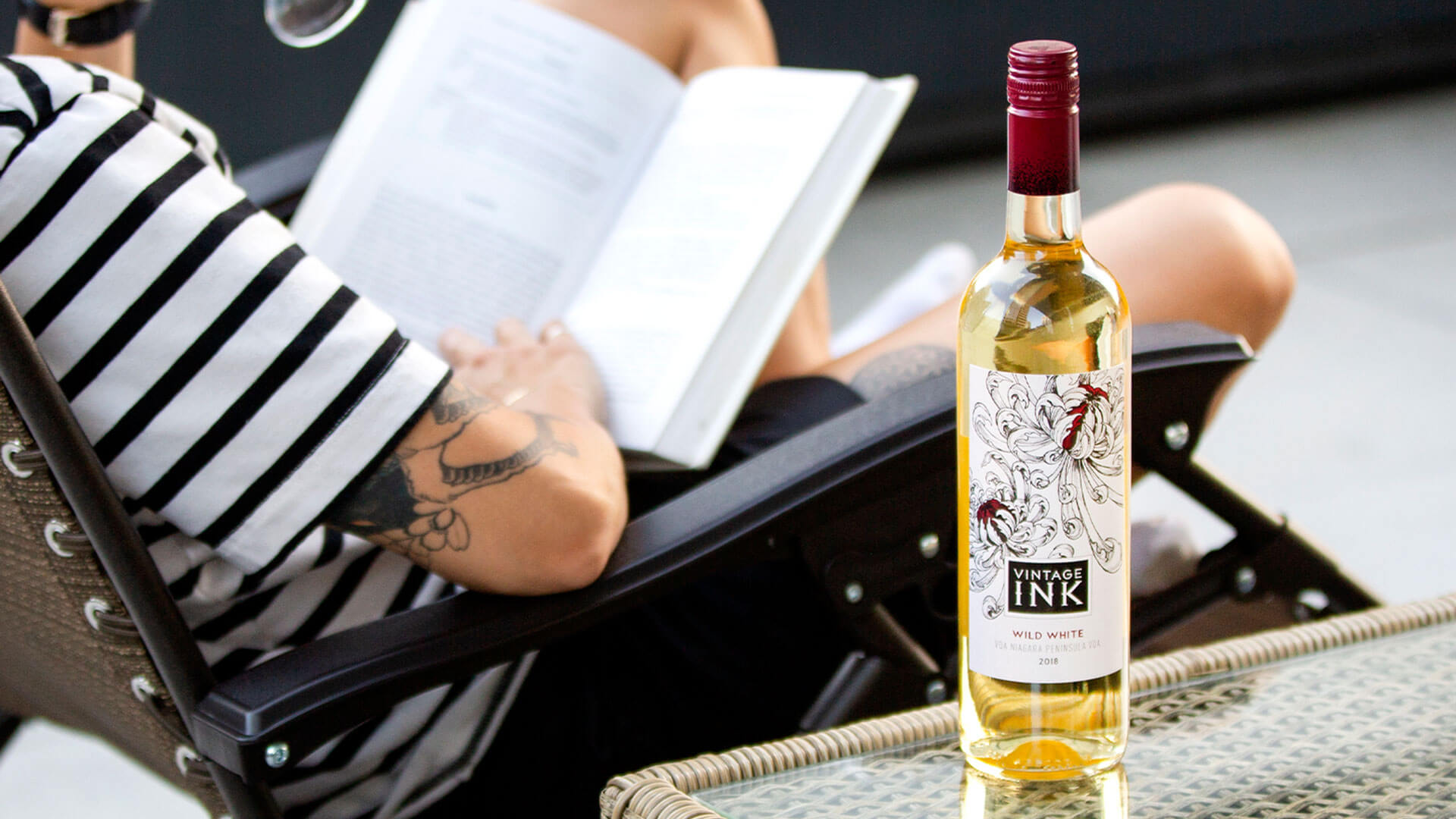 Vintage Ink Wild White 2018 wine bottle on table with wine lover reading a book. 