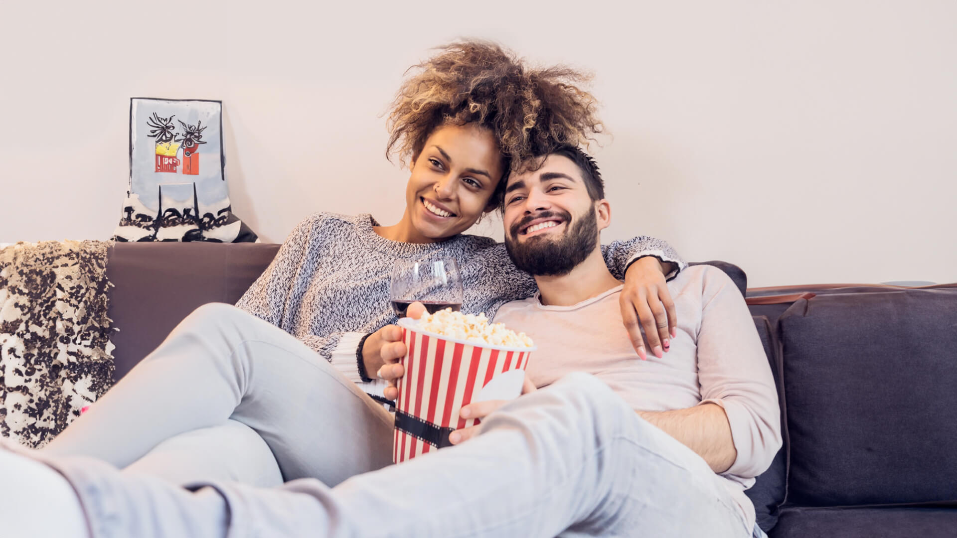 Couple cuddling enjoying popcorn and a glass of red wine. 