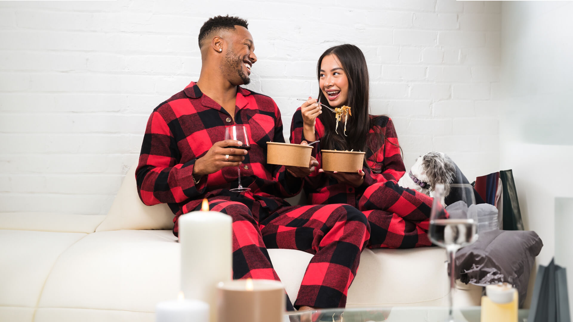 Couple in matching pajamas enjoying dinner and a glass of red wine. 