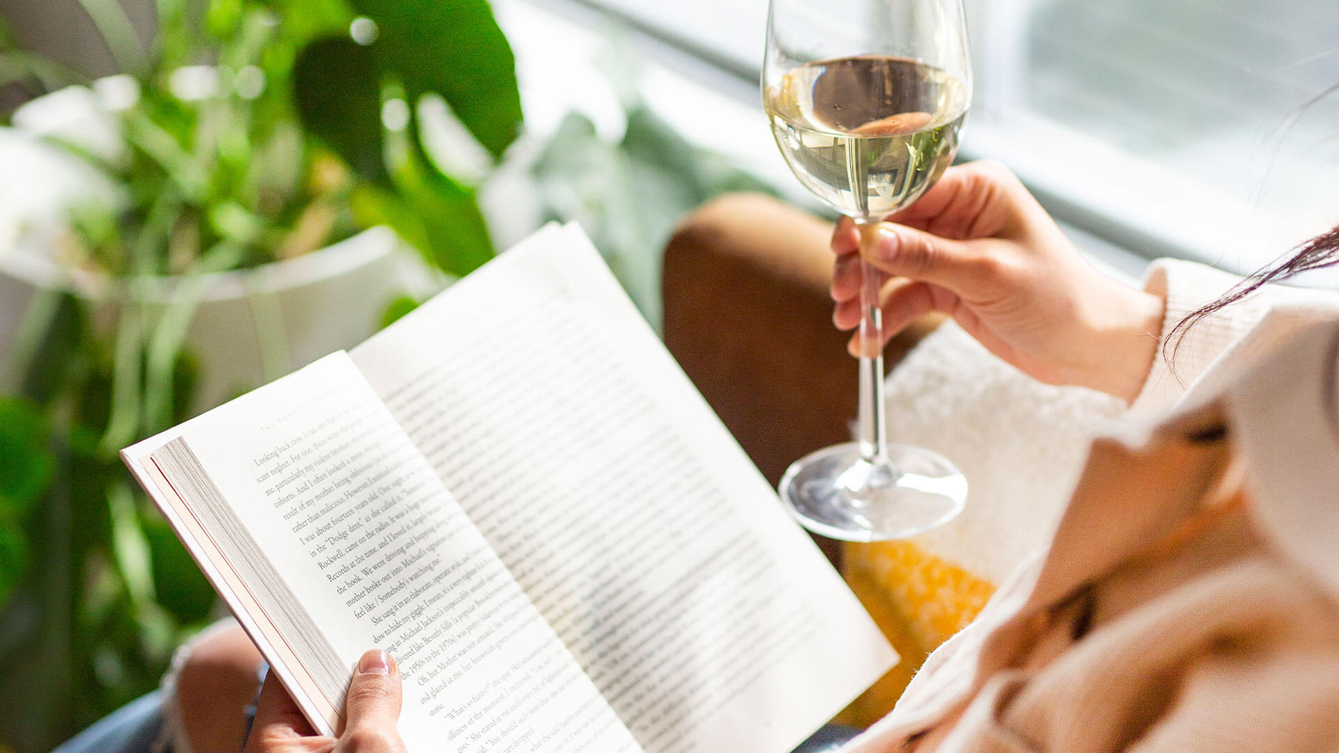 Enjoying a glass of white chardonnay wine while reading inside.