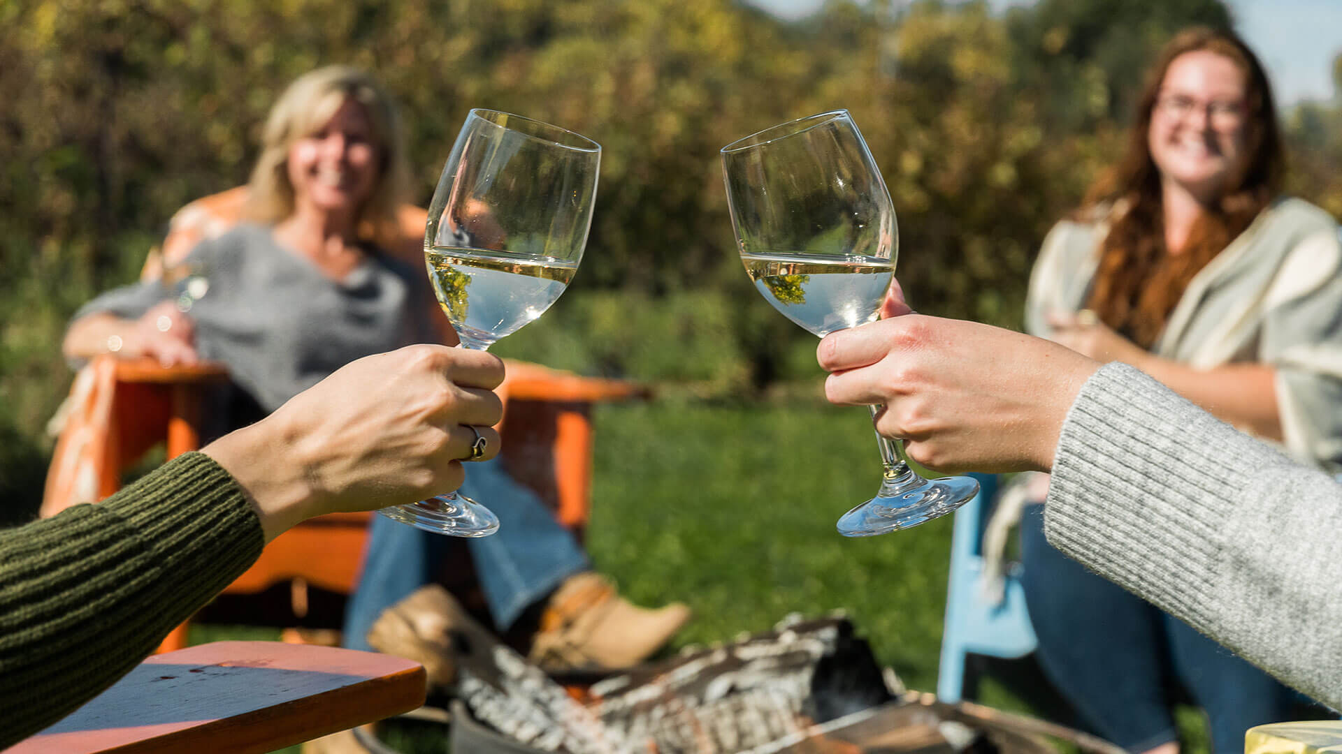 Group of friends celebrating with a glass of white wine while relaxing by a campfire.
