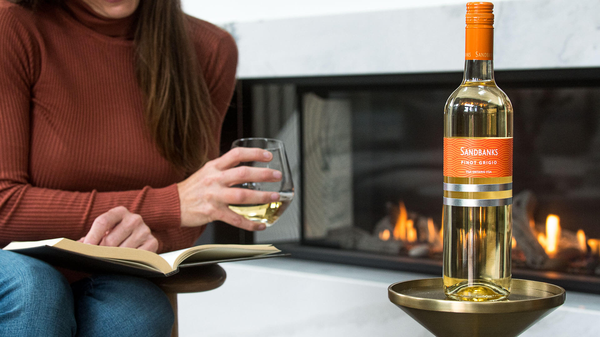 Enjoying a glass of Sandbanks Pinot Grigio VQA white wine while reading by the fireplace.